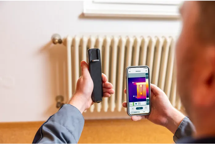 uomo che usa la termocamera con lo smartphone inquadrando un termosifone