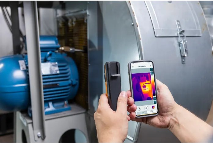 uomo che usa la termocamera con lo smartphone inquadrando un macchinario