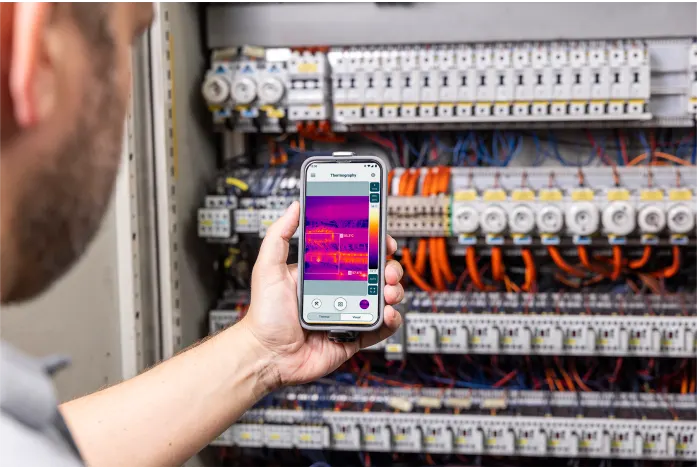 uomo che usa la termocamera con lo smartphone inquadrando un quadro elettrico