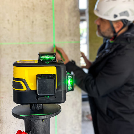 tracciatore in funzione posizionato sopra a treppiede con operaio in cantiere che prende misure